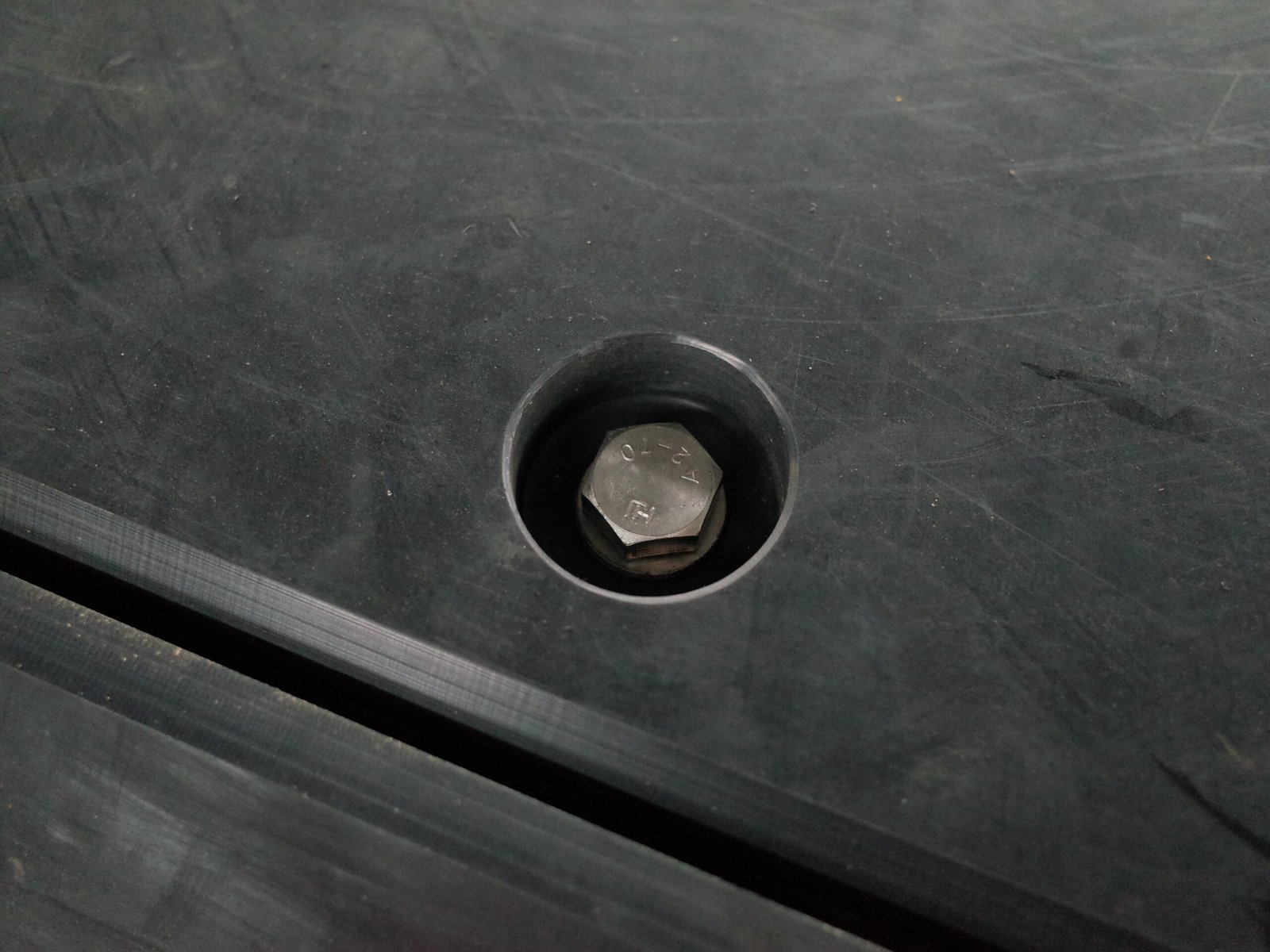 Close view of a recessed hexagonal fixing bolt embedded in a black UHMW-PE pad surface