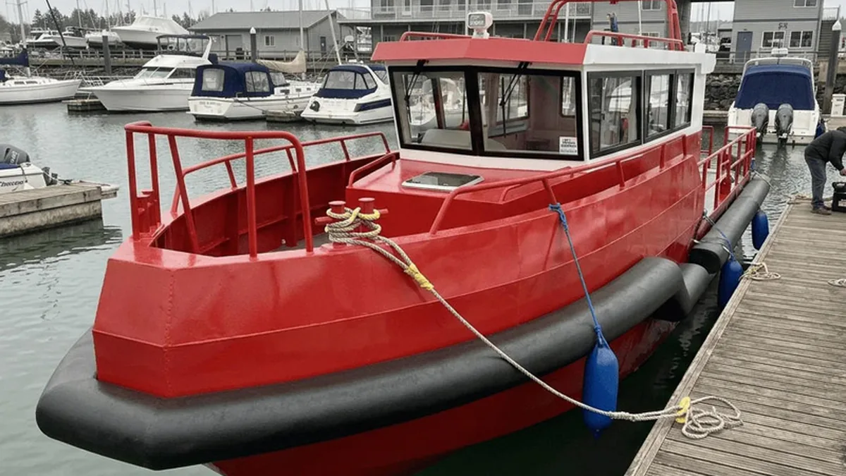 Black foam collar following the bow and side profile of a red workboat at a marina.