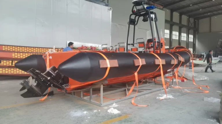 Black foam boat collar fitted around the bow and side of an orange workboat in a workshop.