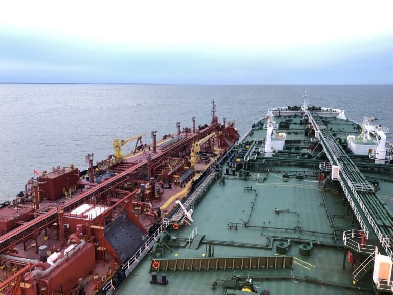 Two tanker vessels positioned alongside each other at sea during a ship-to-ship transfer operation, showing both decks and the vessel-to-vessel interface from an elevated wide angle