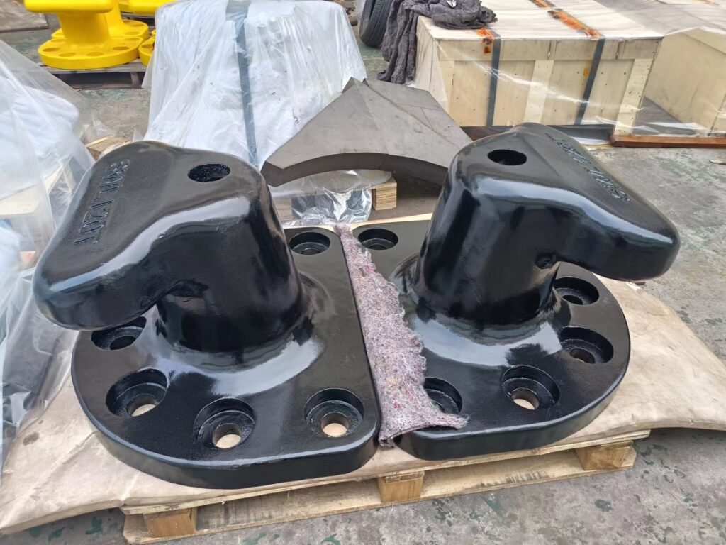 Two black-coated T-head mooring bollards on a pallet, each with a base plate and visible bolt holes